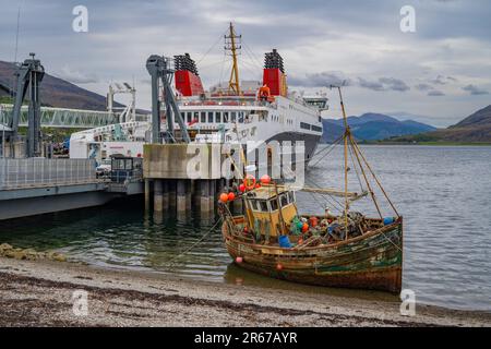 Zerstörtes Fischerboot an der Küste von Ullapool Scotland, mit Loch Seaforth Calmac Fähre hinter sich Stockfoto