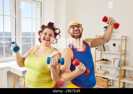 Lustige, übergewichtige, fette Frau mit bärtigem Mann in brillanter Sportbekleidung, die zusammen zu Hause Übungen macht. Stockfoto
