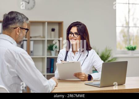 Freundliche Ärztin konsultiert männlichen Patienten beim Ausfüllen des Formulars während der Konsultation. Stockfoto