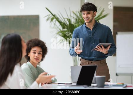 Lächelnder Geschäftsmann Mit Digitalem Tablet, Der Mit Multiethnischen Kollegen In Innenräumen Spricht Stockfoto