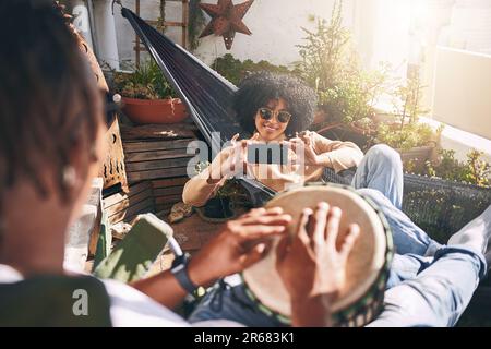 Spielen Sie die Momente ab, halten Sie die Erinnerungen an. Eine junge Frau, die Fotos von ihrem Freund macht, der Schlagzeug spielt. Stockfoto