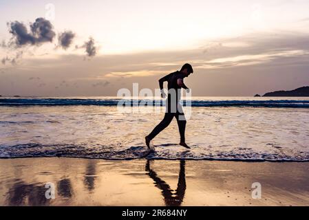 Ein Mann, der bei Sonnenuntergang am Meer vorbeiläuft. Sport am Strand. Stockfoto