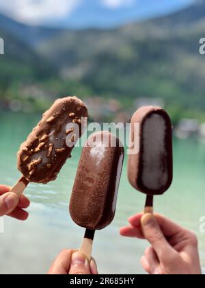 Drei glückliche junge Erwachsene genießen köstliches Schokoladeneis in einer hellen und sonnigen Umgebung im Freien Stockfoto