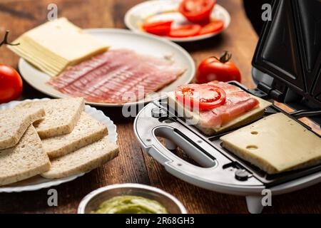 Sandwichmaker und verschiedene Zutaten auf Holzhintergrund. Ich koche Sandwiches. Stockfoto