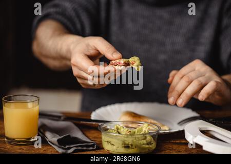 Ein unbekannter Mann isst Toast mit Guacamole. Frühstückszeit. Die Hände des Mannes halten einen Toast. Stockfoto