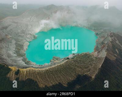 Panoramablick auf die Drohne auf den türkisfarbenen Schwefelwassersee, umgeben von Felsklippen am Vulkan Kawah Ijen. Luftperspektive in Ost-Java, Indonesien. Natürlicher Landschaftshintergrund Stockfoto