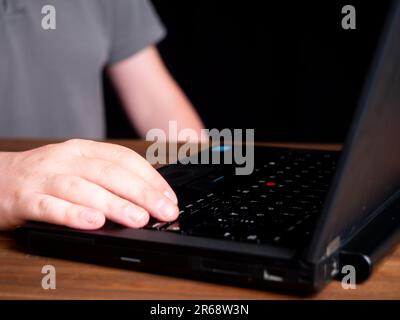Dunkle und launische Aufnahme eines Mannes, der an einem Laptop arbeitet. Nahaufnahme der mobilen Arbeit. Weißer Hintergrund, kein Gesicht. Stockfoto