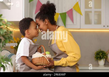 Glückliche afroamerikanische Mutter und ihr süßer Sohn mit Ostereiern, die die Stirn in der Küche berühren Stockfoto