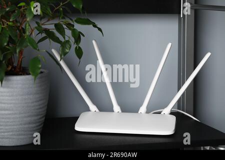 Neuer weißer WLAN-Router in der Nähe einer Topfpflanze auf schwarzem Regal Stockfoto