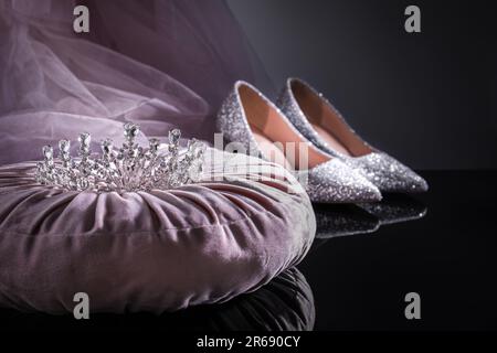 Pinkfarbenes Kissen mit wunderschönem silbernen Diadem neben Schuhen auf schwarzem Tisch Stockfoto