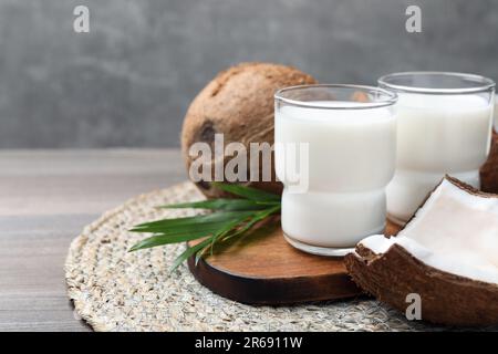 Gläser mit köstlicher Kokosmilch, Palmenblättern und Kokosnüssen auf einem Holztisch, Platz für Text Stockfoto