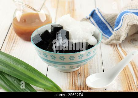 Schwarze Kräuter, Grasgelee mit Kokosnussfleisch, serviert mit Palmenzuckersirup. Cincau Hitam Kelapa, Asiatisches Dessert Stockfoto