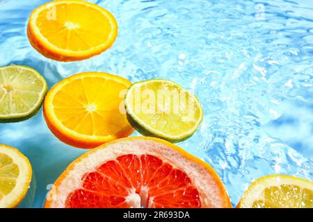 Verschiedene Zitrusfrüchte in Wasser auf blauem Hintergrund Stockfoto
