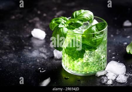 Basilikum: Alkoholisches Cocktailgetränk mit trockenem Gin, Sirup, Zitrone, Basilikum und Eis, dunkler Bartheke-Hintergrund Stockfoto