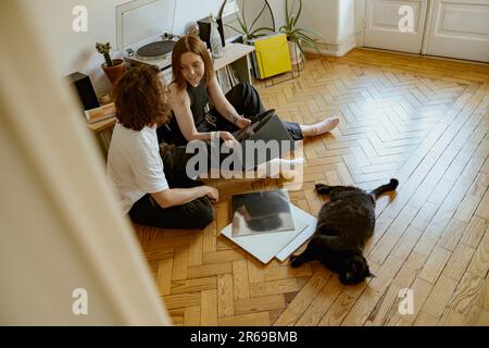 Ein junges Paar sitzt auf dem Boden und hört Musik auf einem Vinyl-Player mit verschiedenen Schallplatten Stockfoto