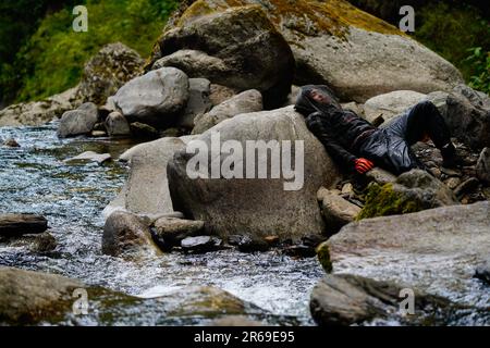 Sindhupalchowk, Nepal. 05. Juni 2023. Ein Honigjäger ruht auf einem Felsen entlang des Flusses Bhotekoshi. In den bezaubernden Hügeln Nepals entfaltet sich eine uralte Tradition namens Honigjagd, während mutige Individuen sich auf der Suche nach dem goldenen Nektar der Natur in die tückischen Klippen wagen. Mit nur einem Seil als Rettungsleine steigen diese Honigjäger in große Höhen und riskieren ihr Leben für die Chance, in den Höhen versteckte Honigwaben zu ernten. Die ländliche Gemeinde Bhotekhosi im Stadtteil Sindhupalchowk dient als ihr gewagter Spielplatz. Kredit: SOPA Images Limited/Alamy Live News Stockfoto