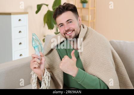 Lächelnder Mann, der den Vernebler zur Inhalation hält und drinnen den Daumen nach oben zeigt Stockfoto