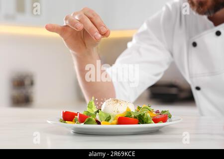 Professioneller Koch salzt köstlichen Salat am Marmortisch, Nahaufnahme Stockfoto