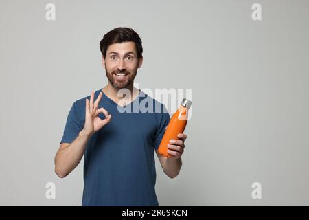 Mann mit orangefarbener Wärmflasche mit OK-Geste auf hellgrauem Hintergrund. Platz für Text Stockfoto