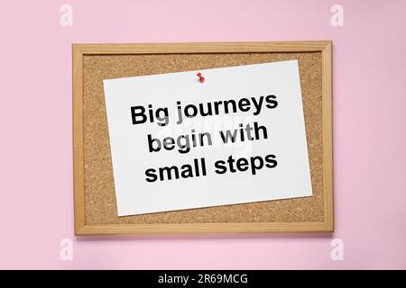 Korkboard mit angehefteter Botschaft große Reisen beginnen mit kleinen Schritten auf pinkfarbenem Hintergrund, Draufsicht. Motivierendes Zitat Stockfoto