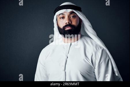 Er ist ein traditioneller Mann und ein Geschäftsmann. Studiofoto eines jungen Mannes in islamischer traditioneller Kleidung, der vor einem dunklen Hintergrund posiert. Stockfoto