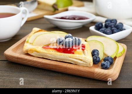 Frisches, leckeres Blätterteig mit Marmelade, Blaubeeren und Birne auf Holztisch, Nahaufnahme Stockfoto