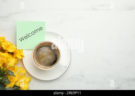 Begrüßungskarte, wunderschöne gelbe Freesia-Blumen und eine Tasse aromatischen Kaffee auf einem weißen Marmortisch, flach liegend Stockfoto