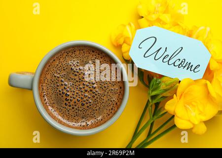 Willkommenskarte, wunderschöne Freesia-Blumen und eine Tasse aromatischen Kaffee auf gelbem Hintergrund, flach liegend Stockfoto