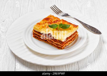 Portion Lasagne al forno, italienische Rinderlasagne mit Rinderhack, Marinara-Sauce, Nudelnudeln und Ricotta-Käse auf weißem Teller mit Gabel Stockfoto