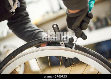 Nicht erkennbarer Fahrradmechaniker mit Schutzhandschuhen, der einen luftlosen Reifen in einer Reparaturwerkstatt von einem Rad entfernt. Selektive Fokuszusammensetzung mit Stockfoto