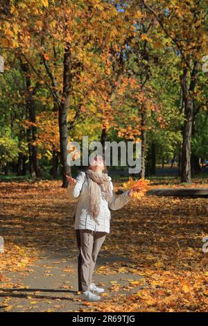 Das Foto wurde im Odessa-Park namens Dyukovsky-Garten aufgenommen. Auf dem Bild fängt ein Mädchen freudig gelbe Blätter, die im Herbst vom Baum fallen Stockfoto