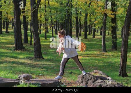 Auf dem Foto springt eine junge Frau im Herbstwald von Stein zu Stein. Stockfoto