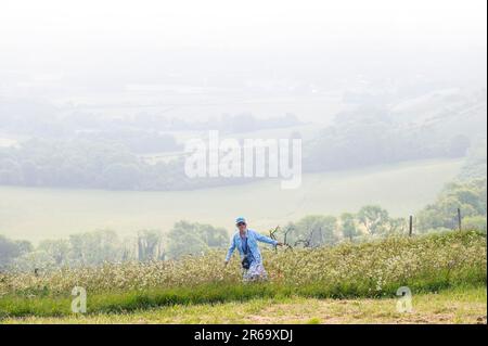 Brighton UK, 8. Juni 2023 - Ein Wanderer beobachtet, wie die Sonne durch den frühen Morgennebel am South Downs Way am Ditchling Beacon bei Brighton zu brennen beginnt, da für die nächsten Tage in ganz Großbritannien heißes Wetter vorhergesagt wird : Credit Simon Dack / Alamy Live News Stockfoto