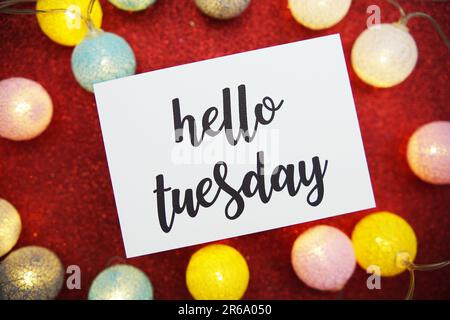 „Hello Tuesday“-Text auf Papierkarte Draufsicht auf rotem Bokeh-Hintergrund Stockfoto