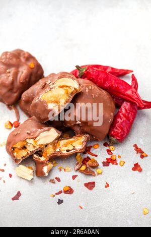 Mit Schokolade überzogene, brüchige Erdnussstücke mit Chili, eine würzige Note auf Grau Stockfoto