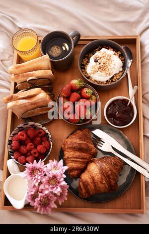 Frühstück im Bett, Top View und Morgenessen mit Croissants, Erdbeeren und Getränken für Wellness, Essen und Hausmannskost. Gastfreundschaft, Hotelmahlzeiten Stockfoto