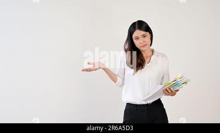 Eine wunderschöne junge asiatische Frau öffnet ihre Hand und hält einen Stapel Papierkram, während sie vor einem isolierten weißen Hintergrund steht und sich frei fühlt Stockfoto