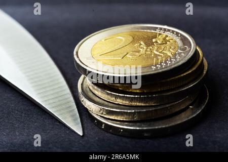 Messerklinge auf Euro-Münze gelegt, Taschenrechner. Konzeptkürzungen, Geldgeschäfte, Verbrechen. Makro. Stockfoto