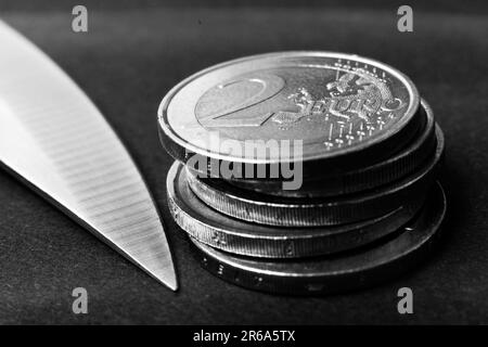 Messerklinge auf Euro-Münze gelegt, Taschenrechner. Konzeptkürzungen, Geldgeschäfte, Verbrechen. Makro. Stockfoto