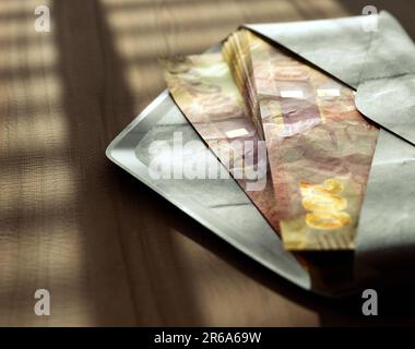 Ein Stapel rand-Banknoten in einem Umschlag auf einer Holzfläche unter stimmungsvoller Beleuchtung - 3D-Darstellung Stockfoto