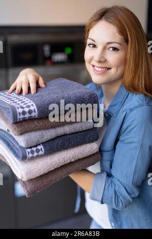 Eine aufgeweckte junge Dame hält einen Stapel gefalteter Handtücher Stockfoto