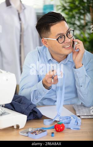 ein asiatischer Schneider ruft an und spricht über Modekleidung Stockfoto