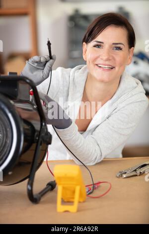 Eine glückliche Elektrikerin misst die Spannung eines Geräts Stockfoto