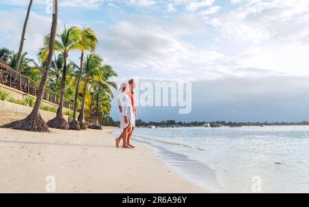 Ein Paar, das sich am exotischen Sandstrand umarmt, während es einen Abendspaziergang am Strand von Trou-aux-Biches auf Mauritius macht und den Sonnenuntergang genießt. Die Beziehung zum Menschen Stockfoto