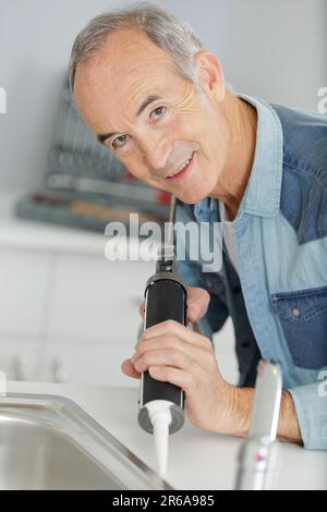 Senior repariert einen undichten Wasserhahn Stockfoto