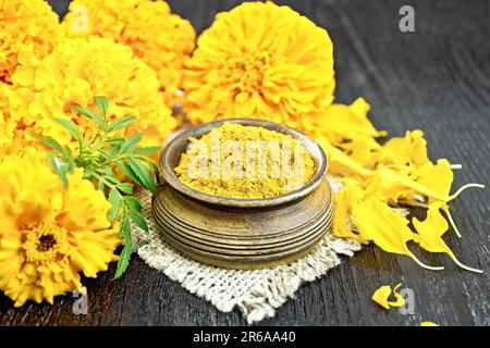 Imerezianischer Safran in einer Schüssel auf Leinenholz, Blütenblättern und frischen Tagetes-Blumen auf Holzbretterhintergrund Stockfoto