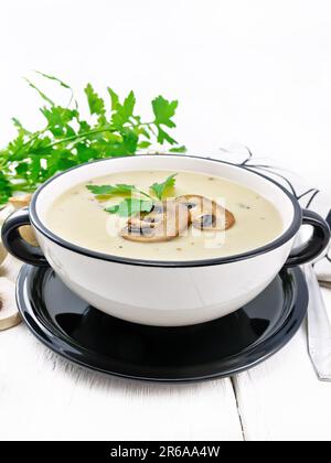Suppenpüree aus Champignons, Kartoffeln, Zwiebeln und Sahne in einer Schüssel, einer Serviette, Petersilie und einem Löffel auf Holzbrettuntergrund Stockfoto