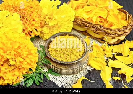 Imertinisches Safran in einer Schüssel auf Leinenholz, Tagetes-Blüten in einem Korb aus Korb und auf dem Tisch, frische Tagetes-Blüten auf dunklem Holzbrett-Hintergrund Stockfoto