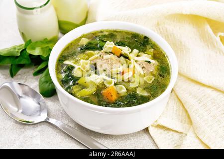 Italienische Suppe Ministra Maritata mit Fleischbällchen, Spinat, Karotten, Petiolsellerie und feiner Pasta in einer Schüssel, Serviette und Löffel auf Granithintergrund Stockfoto