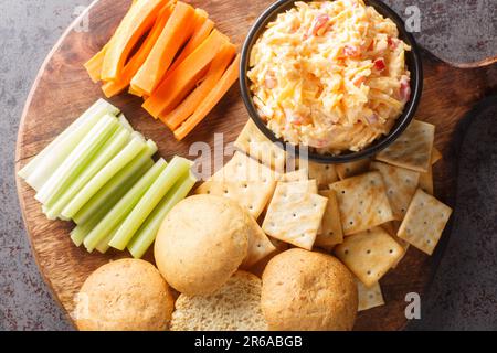 Pimento-Käse mit Sellerie, Karottenstäbchen und Crackern auf dem Holzbrett auf dem Tisch. Horizontale Draufsicht von oben Stockfoto